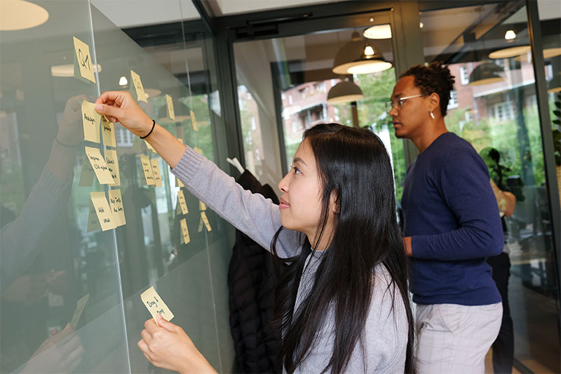 woman in gray long sleeve shirt pasting sticky notes to board