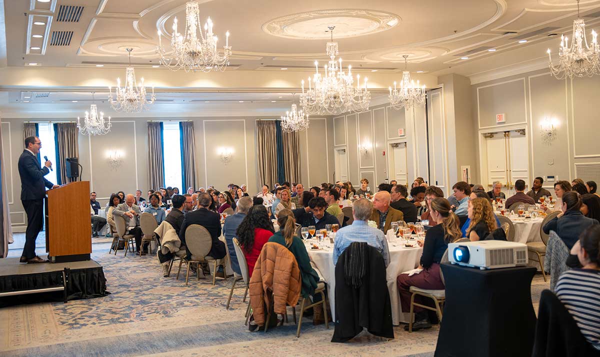 attendees seated around tables listen to presentation at luncheon