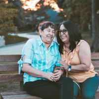 two women sitting on a park bench and smiling, one older, one younger